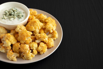 Homemade Buffalo Cauliflower with Blue Cheese Sauce on a Plate on a Black Background, side view. Copy space.