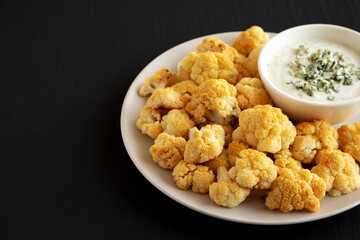 Homemade Buffalo Cauliflower with Blue Cheese Sauce on a Plate on a Black Background, side view. Copy space.