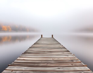 Fototapeta premium A weathered wooden pier extends out into a still, foggy lake, with trees displaying brilliant autumn colors lining the far shore.