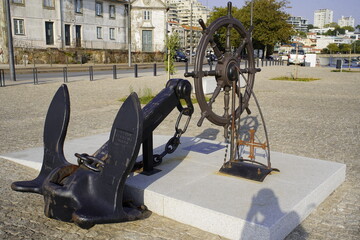 Old ship anchor and ship steering wheel in the harbor of Porto, Portugal.