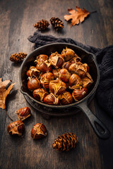 Roasted edible sweet chestnuts in iron pan on wooden table