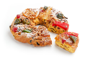 A partially sliced wreath shaped cake decorated with candied fruit, nuts, and powdered sugar