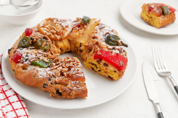 A festive wreath shaped cake with candied fruit, nuts, and sugar, displayed on a white plate