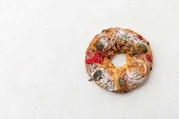 A simple wreath shaped cake with candied fruit and nuts, displayed on a white surface