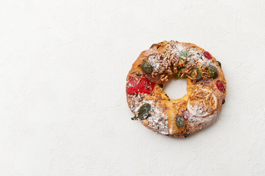 A simple wreath shaped cake with candied fruit and nuts, displayed on a white surface