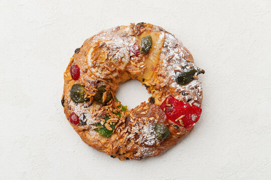 A top down view of a festive wreath shaped cake decorated with candied fruit and nuts on a white plate