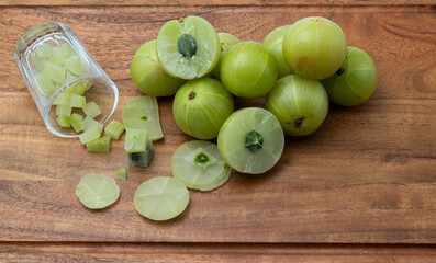 A glass of Amla juice ,chopped amla and whole amla also known as Indian gooseberry placed on a wooden chopping board.