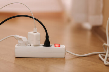 White cable connector for overloaded power boards at home. Close up focus at a plug foreground.