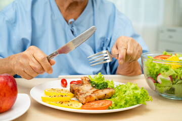 Asian elderly woman patient eating salmon stake and vegetable salad for healthy food in hospital.