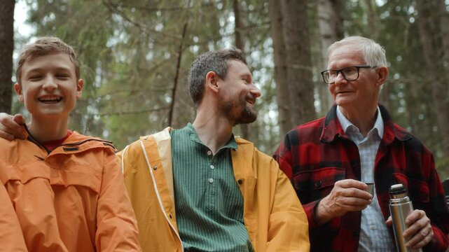 Grandfather, son and teenage grandson in forest. Three male family generations. Elderly and adult man, and boy sitting on bench and drinking tea from thermos to have rest. Enjoy chatting and strolling