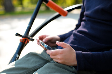 Schoolboy plays on his phone while sitting on bench in city park. Boy uses mobile gadget to communicate with friends while outdoors on sunny day. Children are addicted to Internet.