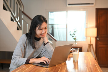 Beautiful young female freelancer working with her laptop in cozy kitchen