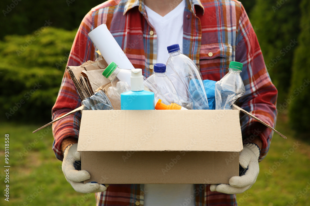 Wall mural Recycling. Man holding cardboard box with different garbage outdoors, closeup