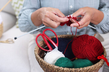 Woman with basket of yarn knitting at home, closeup