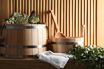 Sauna equipment. Buckets, whisks, ladle, and towel on bamboo bench near wooden wall