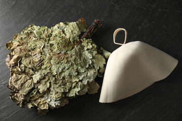 Sauna equipment. Oak whisk and felt wool hat on black textured surface, flat lay