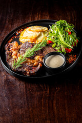 A close-up of a gourmet steak dinner with sauce and a side salad on a dark plate, highlighting the textures and vibrant colors. Perfect for food photography, restaurant menus, or culinary blogs.