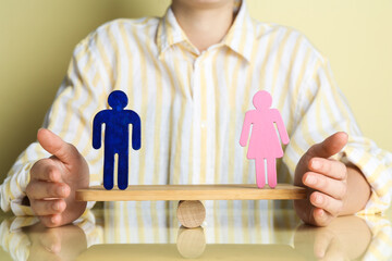 Gender equality concept. Woman with male and female figures on scales against light yellow...