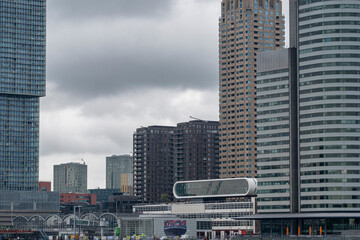 Multiple high-rise buildings and skyscrapers stand against a cloudy sky, showcasing modern architecture and urban construction in a densely built cityscape  in Rotterdam