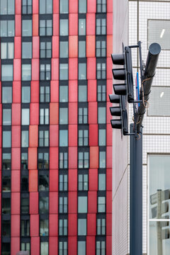 A close-up view of a modern building with red and black checkerboard-pattern facades, featuring rows of windows and traffic lights in an urban environment.