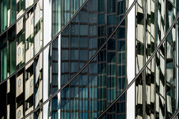 An abstract view of reflections in a mirrored glass facade of an urban building, depicting various angles and distortions with a play of light and architecture.