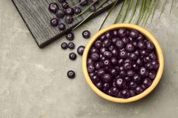 Ripe acai berries in bowl on grey textured table, flat lay. Space for text