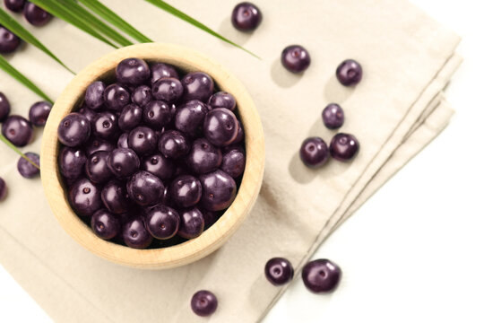 Ripe acai berries in bowl on white table, flat lay