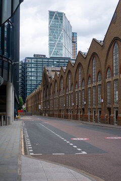 A row of classic brick industrial buildings with repetitive arched windows contrasts with a modern glass-cased tower in the background, showcasing historical and contemporary elements in London