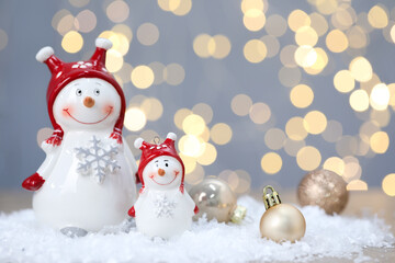 Funny snowmen figure and Christmas balls on artificial snow against blurred lights