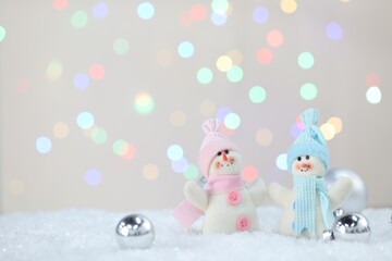 Cute snowmen and Christmas balls against beige background with blurred lights, bokeh effect