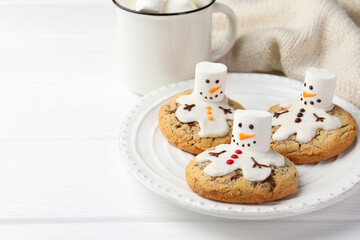 Delicious cookies with snowmen made of marshmallows on white table, closeup. Space for text