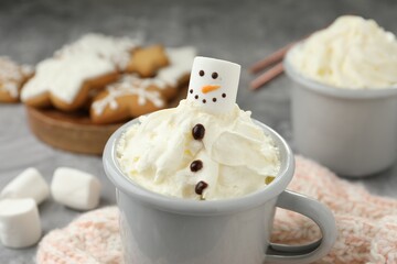 Funny snowman made with marshmallow and whipped cream in cup of hot drink served on grey background, closeup