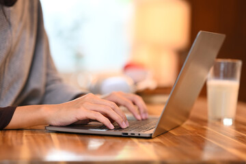 Close up shot of young woman typing on laptop keyboard at wooden kitchen table