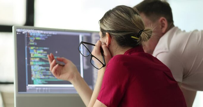 Woman shows program coding on computer monitor to man colleague in office. Partners examine coding errors and bugs on computer screen slow motion
