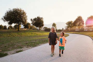 Sister and little brother walking along a park path on a warm sunny day