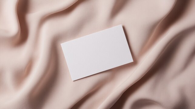 A blank business card rests on soft, textured fabric, creating a minimalist and elegant aesthetic.