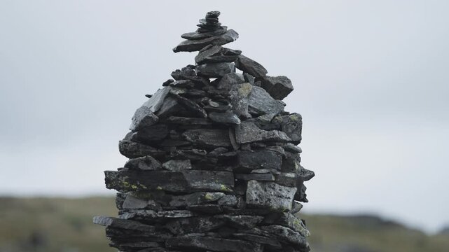 A stone cairn made of dark jagged pointy rocks in the gloomy landscape. Parallax video.