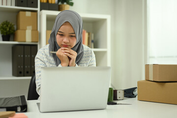 Asian Muslim woman small business owner using laptop for online marketing or checking purchase order