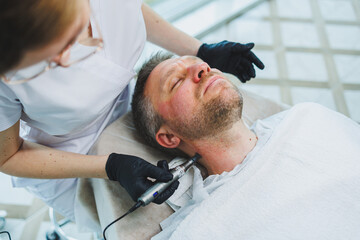 Fototapeta premium A beautician makes a mask on the face of a man with a beard. Male cosmetology. Preservation of youth and facial skin care. Beauty salon concept.