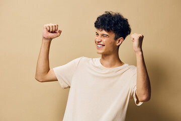 Happy young man celebrating success with raised fists, joyful expression, on a soft beige background A vibrant moment capturing enthusiasm and positivity