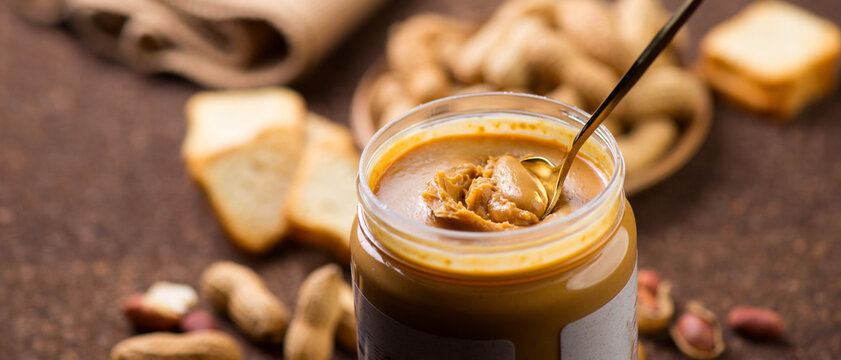 Peanut butter. Creamy smooth peanut butter in jar on a table. Spoon of natural organic vegan food. American cuisine 