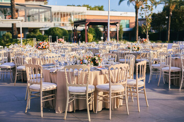 Elegant Outdoor Wedding Reception with Draped Canopy, Floral Centerpieces, and White Chairs...