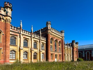 Naklejka premium A wide-angle shot of a grand historic estate with intricate Gothic architecture, featuring tall arched windows and decorative towers. The scene is set on a sunny day with a vibrant blue sky
