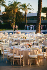 Elegant Outdoor Wedding Reception with Draped Canopy, Floral Centerpieces, and White Chairs Next to a Swimming Pool Overlooking a Waterfront Venue