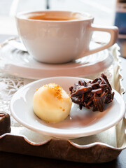 A white cup of coffee sits next to a plate of chocolate covered almonds