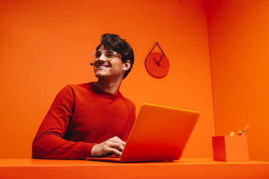 Smiling millennial man working as a customer support agent in a vibrant, monochromatic orange workspace