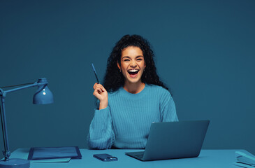 Confident female student laughing while working on laptop in monochromatic office setup