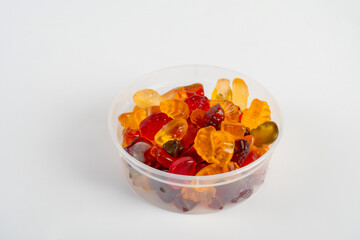 Fruit flavored worm shape, jelly candies in white cup. Isolated on cream background.