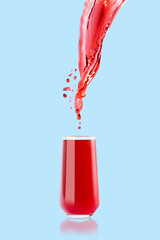 Red cherry juice. Stream of drink flow in drinking glass with bright splashes, drops flying, swirl on blue background. Vitamin cocktail with splashing for advertising, design, flyer, poster, card.