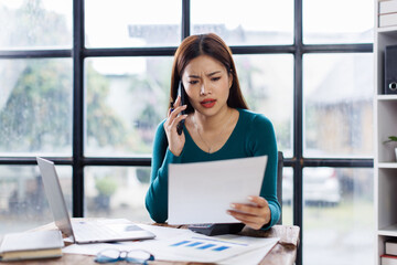 Asian woman entrepreneur busy with her work in the office. Young Asian woman work on desk laptop phone while planning sales, research or financial strategy in company
